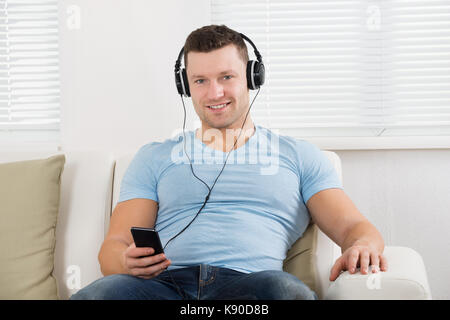 Portrait of mid adult man listening to music on mobile phone at home Banque D'Images