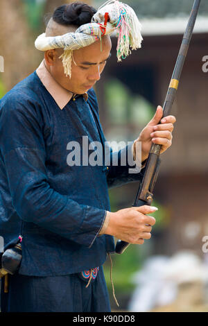 Biasha, Chine - 17 septembre 2007 : l'homme des minorités ethniques Miao en bleu, vêtements traditionnels et de longs cheveux coiffure tressée bun chargement du fusil à Miao vi Banque D'Images