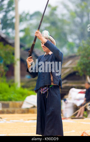 Biasha, Chine - 17 septembre 2007 : l'homme des minorités ethniques Miao en bleu, vêtements traditionnels et de longs cheveux coiffure tressée bun le tournage d'un fusil dans l'air Banque D'Images