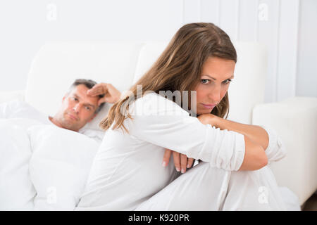 Femme en colère assis sur le lit avec l'homme dans l'arrière-plan Banque D'Images
