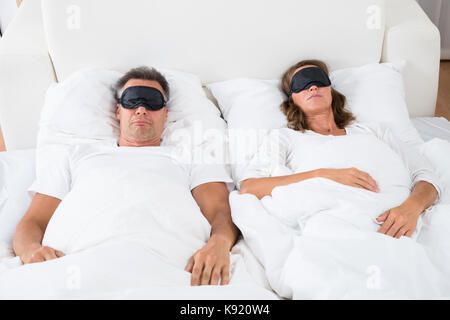 Portrait de mûri Couple confortablement sur lit à l'aide de masque pour les yeux Banque D'Images