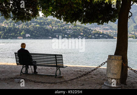 Homme âgé assis sur un banc de parc sur la rive du lac de Côme, Italie Banque D'Images