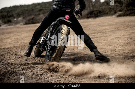 Vue arrière Vue de l'homme section faible circonscription cafe racer moto sur une route de terre poussiéreuse. Banque D'Images