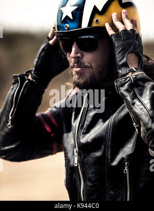 Homme barbu portant veste en cuir noire et des lunettes de réglage de son casque open face jaune. Banque D'Images