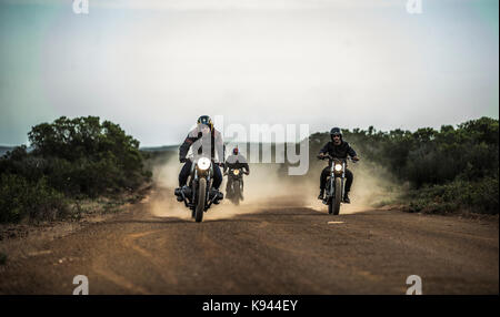 Trois hommes à cheval cafe racer motorcycles le long chemin de terre poussiéreux. Banque D'Images