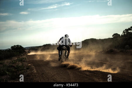 Vue arrière de l'homme équitation cafe racer moto sur une route de terre poussiéreuse. Banque D'Images