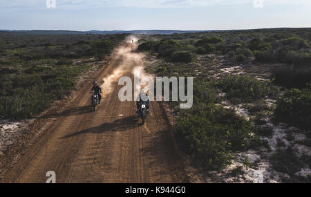 Paysage avec deux hommes circonscription cafe racer moto dans des cercles sur une route de terre poussiéreuse. Banque D'Images