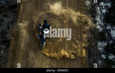 Portrait de l'homme conduisant cafe racer moto dans des cercles sur une route de terre poussiéreuse. Banque D'Images