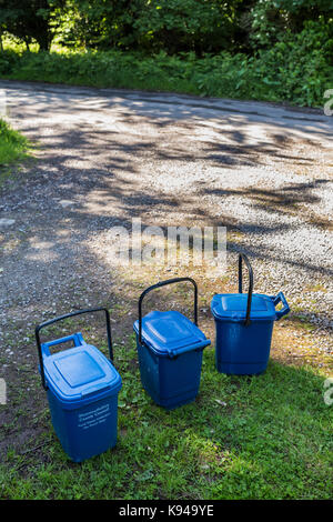 Des poubelles en plastique bleu collection en attente sur une étroite route de campagne monmouthshire, Wales. Banque D'Images