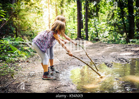 Enfants randonnées en montagne ou forêt avec des chaussures de randonnée sport. les filles jouent et l'apprentissage dans la nature avec des bâtons et boueux flaque. Banque D'Images