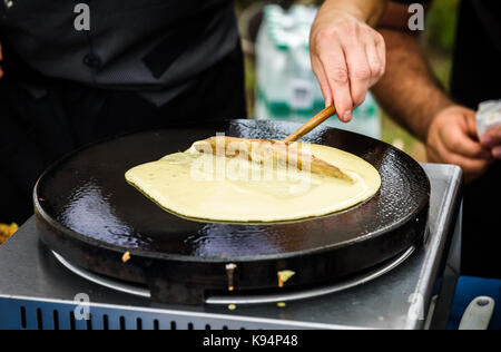 Faire des crêpes crêpes au marché libre. juste une part du festival est de faire des crêpes à l'extérieur sur une plaque en métal avec manche en bois sur une terrasse extérieure d'fest Banque D'Images