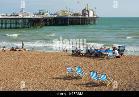 Des gens assis sur la plage de galets à Brighton dans l'East Sussex, Angleterre. avec pier en arrière-plan Banque D'Images