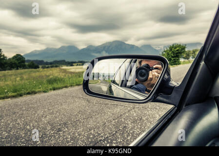 Réflexion d'un photographe avec un appareil photo dans le rétroviseur d'une voiture. Banque D'Images