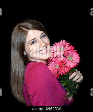 Transmission de jeune femme est titulaire d'bouquet de marguerites rose. Elle est proche de bouquet agrippant son visage. fond est noir et l'objet est en coin pour copier Banque D'Images