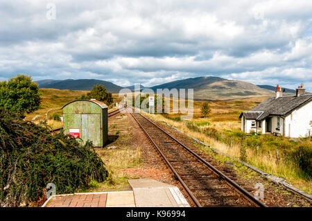 Un crofter's Cottage peint blanc reflète le soleil d'automne comité permanent par des lignes de chemin de fer de quitter la plate-forme des montagnes au loin vers la station de Rannoch Banque D'Images