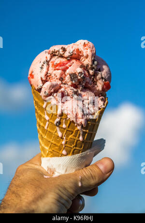Photo verticale d'un homme de race blanche main tenant un cornet de crème glacée qui est en train de fondre contre un ciel bleu avec des nuages blancs Banque D'Images