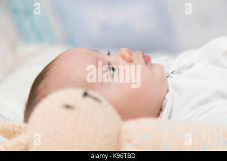 BÉBÉ AVEC MANNEQUIN. Bébé garçon reposant sur le lit avec un mannequin de lapin en crochet de côté. Vue latérale de la face. Banque D'Images