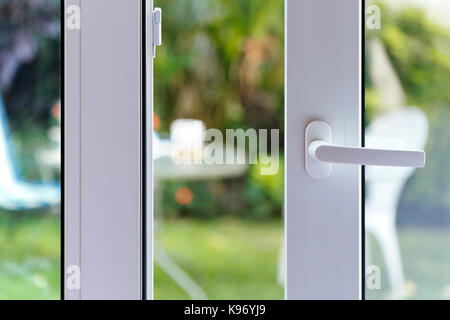 Ouvrez la porte d'une maison familiale. Close-up de la serrure de porte coulissante avec la cour d'arrière-plan. Porte en PVC blanc et double vitrage. Banque D'Images