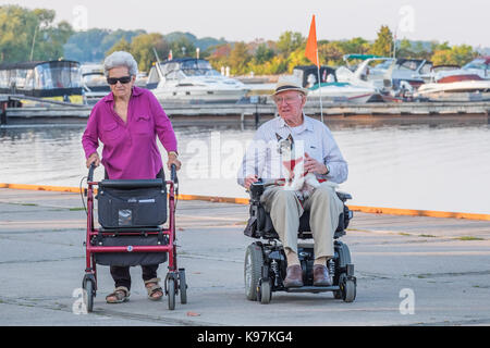 Couple de personnes âgées bénéficiant d'une soirée de fin d'été au coucher du soleil, elle dans un fauteuil roulant et elle avec une marchette. Banque D'Images