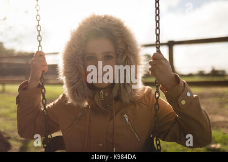 Portrait of young woman wearing winter coat swinging in playground Banque D'Images