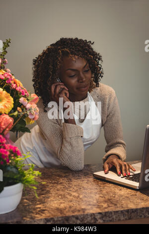 Female florist taking order sur son ordinateur portable à la boutique de fleur Banque D'Images