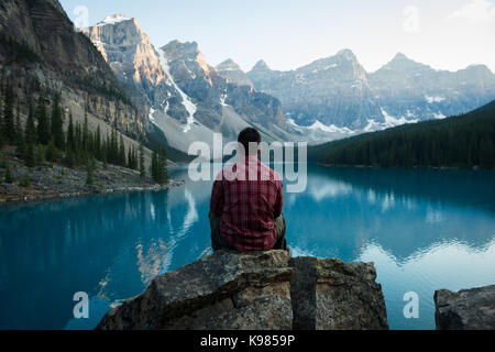 Vue arrière de l'homme assis près de côté lac sur une journée ensoleillée Banque D'Images