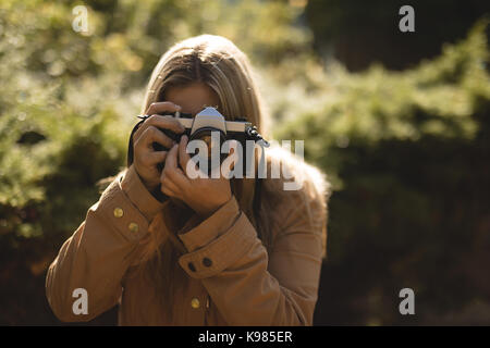Young woman photographing manteau d'hiver avec l'appareil photo du park Banque D'Images