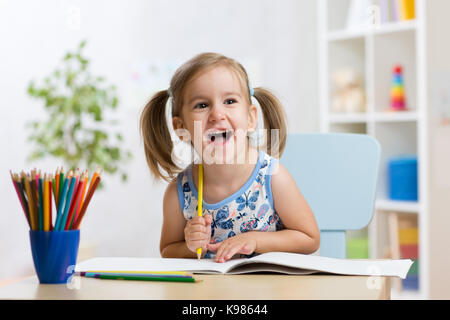 Fille enfant expressif attire l'assis à table dans la salle à la maternelle Banque D'Images