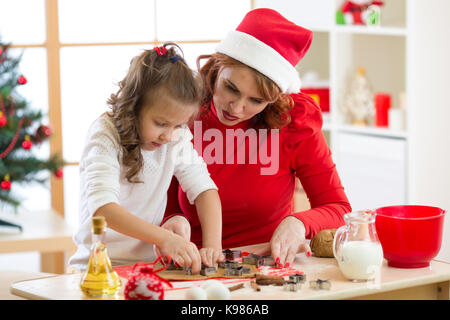 Heureuse femme et enfant fille coupant les cookies de noël hors de pâte ensemble Banque D'Images