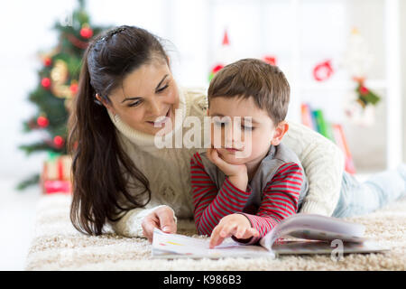 Prendre soin mère lit à son enfant un livre intéressant la veille de Noël Banque D'Images