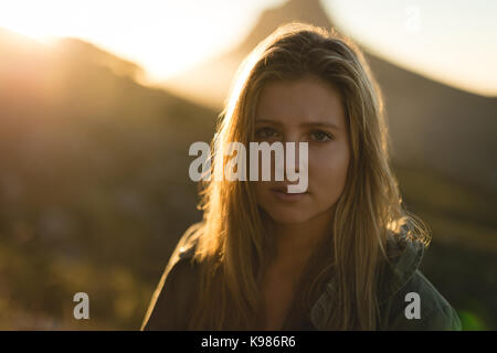 Portrait of young woman standing contre mountain pendant le coucher du soleil Banque D'Images