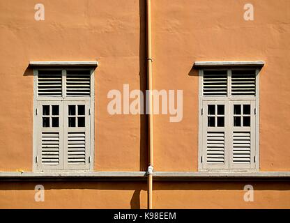 Une paire de fenêtres traditionnelles avec des volets en bois séparés par un tuyau d'eau vertical sur le côté d'une maison près de Orchard Road, à Singapour