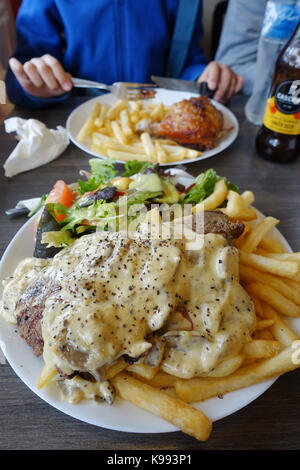 Une assiette de steak avec une sauce aux champignons et frites avec un bol de salade grecque et poulet schnitzel burger dans l'arrière-plan Banque D'Images