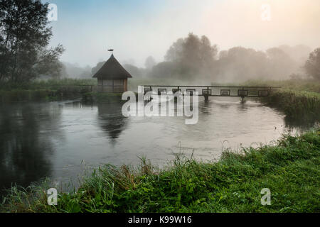 Le soleil perce la brume sur la rivière Eel Test Pont piège, Longstock, Hampshire, Royaume-Uni. Banque D'Images