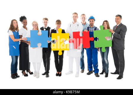 Portrait of smiling people avec diverses professions holding jigsaw pieces tout en standing against white background Banque D'Images