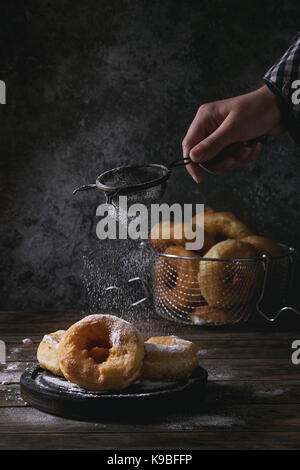 Beignets faits maison avec du sucre en poudre par aspersion en grille vintage enfant part sur noir servant de sélection et en panier sur la vieille planche en bois table. dar Banque D'Images