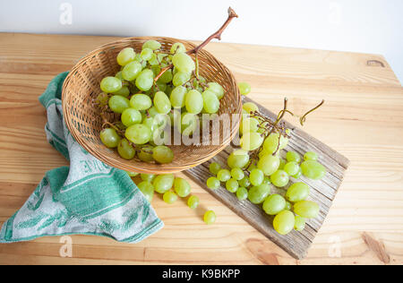 Les grappes de raisins blancs dans un panier de paille sur une planche de bois. Banque D'Images