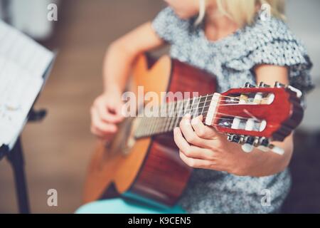 Petite fille d'apprendre à jouer de la guitare à la maison. Selective focus sur la chaîne. Banque D'Images