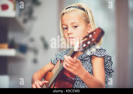 Petite fille d'apprendre à jouer de la guitare à la maison. Banque D'Images