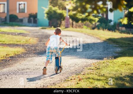 L'été à la campagne. little boy riding scooter push en journée ensoleillée. Banque D'Images