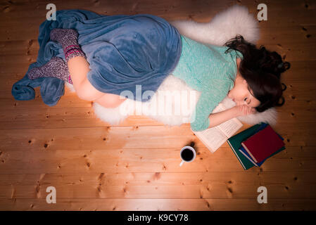 Belle jeune femme s'endormit tout en étudiant, assis sur une fourrure blanche, sur le sol, entourés de livres et d'une tasse de thé. Banque D'Images