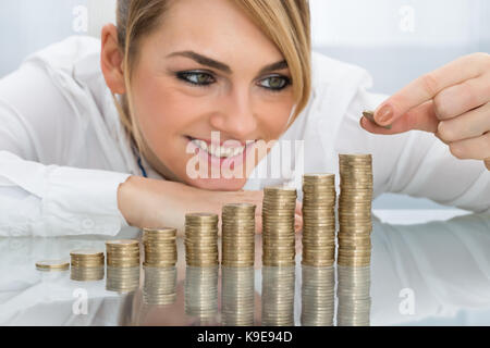 Young businesswoman putting coin sur la pile de pièces d'or Banque D'Images