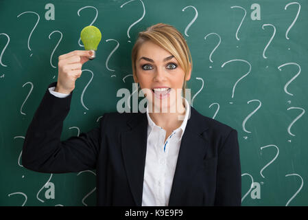 Smiling young businesswoman in front of chalkboard holding ampoule écologique Banque D'Images