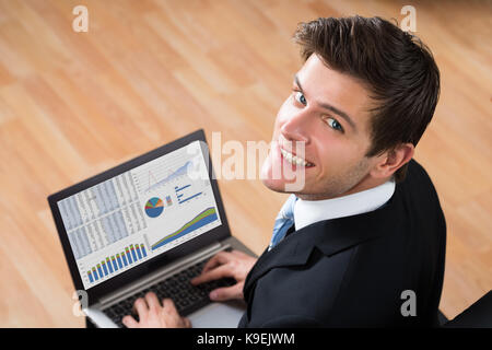 Young happy businessman analyser des données statistiques sur le laptop in office Banque D'Images