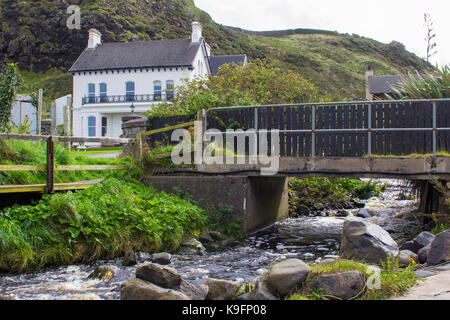 Une maison et un jardin bien entretenus avec une rivière passant sous un petit pont. Situé sur le front de mer à Downhill dans le comté de Londonderry, N. Banque D'Images