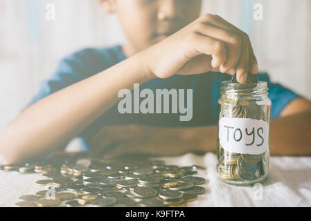 Young Asian boy putting coins into glass jar. économiser de l'argent pour acheter des jouets. La sauvegarde de concept Banque D'Images