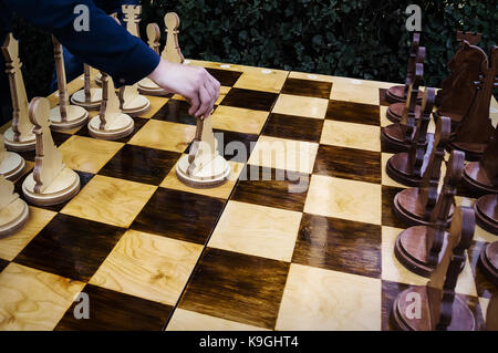 Le jeu d'échecs. le début de la partie. Le premier pas dans les échecs, e2 - e2 le pion blanc. La figure dans les mains de l'homme. grand jeu d'échecs en bois Banque D'Images