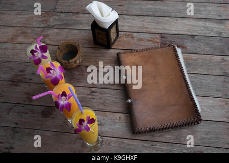 Des boissons colorées ramé jusqu'à une vieille table en bois rustique avec un menu, cendrier et porte-papier sur elle Banque D'Images