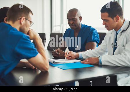 Les jeunes d'un personnel médical des gens assis à table dans la salle de réunion, à quel médecin homme en blouse blanche l'écriture des notes de journal Banque D'Images