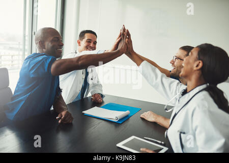 Groupe de jeunes de l'équipe de spécialistes médicaux des cinq plus table que pour accroître l'esprit d'équipe, assis en face de l'autre et souriant Banque D'Images
